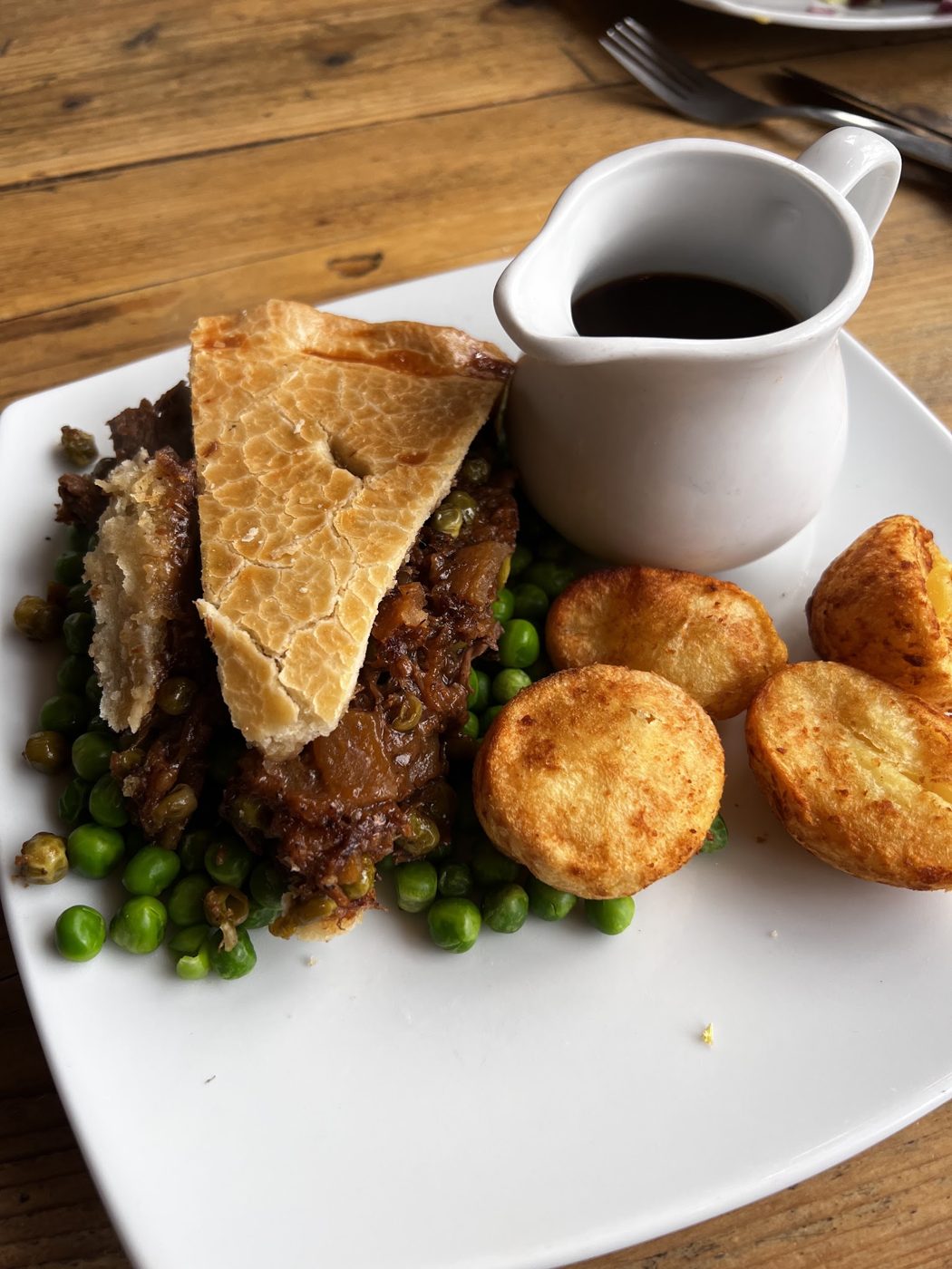 A pie with potatoes, peas and a jug of gravy